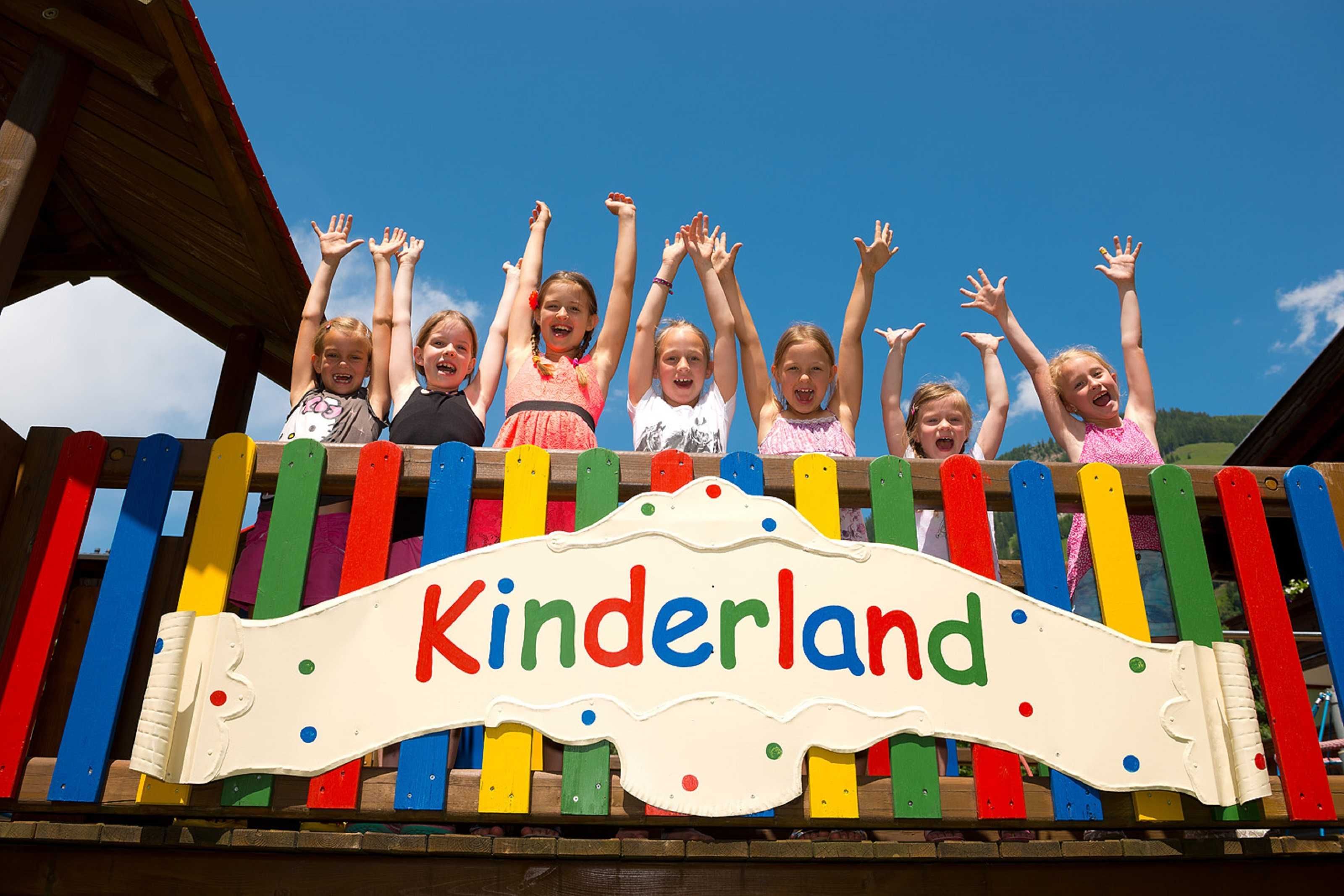 Children on a colorful wooden structure with a sign reading 'Kinderland.'