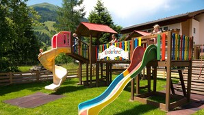 Un parque infantil con toboganes y estructuras para escalar, rodeado de vegetación y un edificio con un letrero que dice 'Kinderland'.