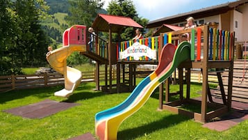 En legeplads med rutsjebaner og klatrestrukturer, omgivet af grønt og en bygning med skiltet 'Kinderland'.