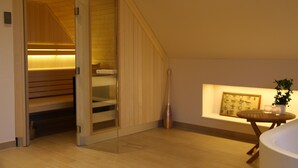 Una habitación moderna con techo inclinado de madera, un banco empotrado, una mesita con una planta y un cuadro en la pared.