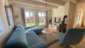 Una sala moderna con sofá, sillón y una pequeña mesa de centro. Hay una chimenea, un televisor y una ventana con cortinas.