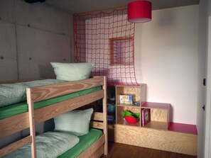 A bunk bed with green bedding, a red hanging lamp, a wooden shelf with books and a red object, and a red netted window. - The Playful (11) - Z1-THE HOUSE (Zwenkau)