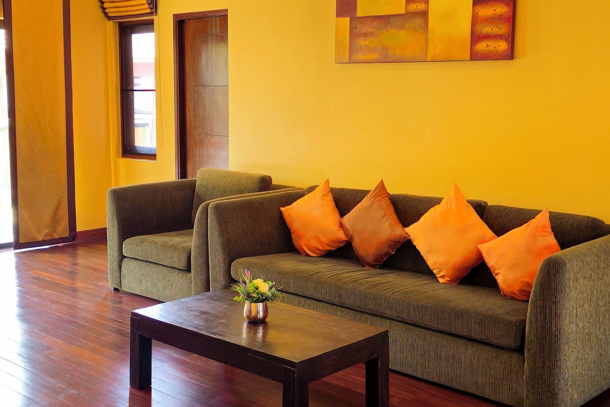 A living room with a green sofa, orange cushions, a wooden coffee table, and a painting on the wall.