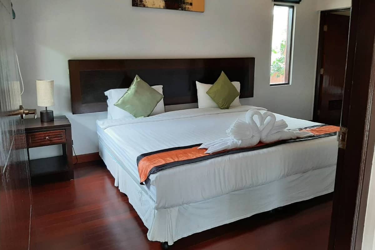 A neatly made bed with a swan towel arrangement, a bedside table with a lamp, and a painting on the wall.