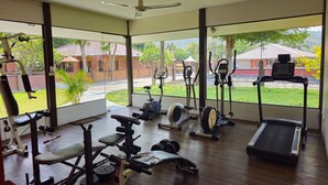 A spacious gym with various exercise equipment, large windows offering a view of the outdoors, and a ceiling fan. - Baan Me Suk Spa & Resort Hua-Hin (Cha-am)