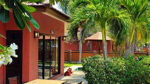 A patio with a table and chairs, a red building with glass doors, and a palm tree. - Baan Me Suk Spa & Resort Hua-Hin (Cha-am)