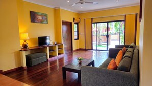 A living room with a sofa, a coffee table, a TV on a stand, and a sliding glass door leading to a patio. - Baan Me Suk Spa & Resort Hua-Hin (Cha-am)