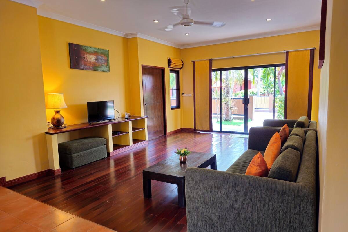 A living room with a sofa, a coffee table, a TV on a stand, and a sliding glass door leading to a patio.