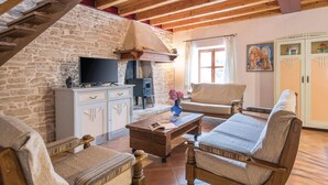 A cozy living room with a stone wall, wooden beams, a fireplace, a television, and a sofa.