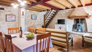 A rustic dining area with a stone wall, wooden beams, a fireplace, and a television.
