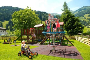A playground with various play structures, including a climbing net, slides, and a wooden playhouse. - Rauriser Jungle Family Studio - Hotel Alpina **** (Rauris)