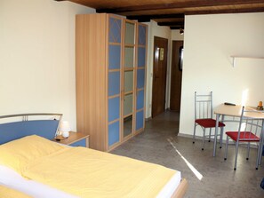 Ein Schlafzimmer mit Bett, Kleiderschrank, Schreibtisch mit Stühlen und einem Flur, der in einen anderen Raum führt.