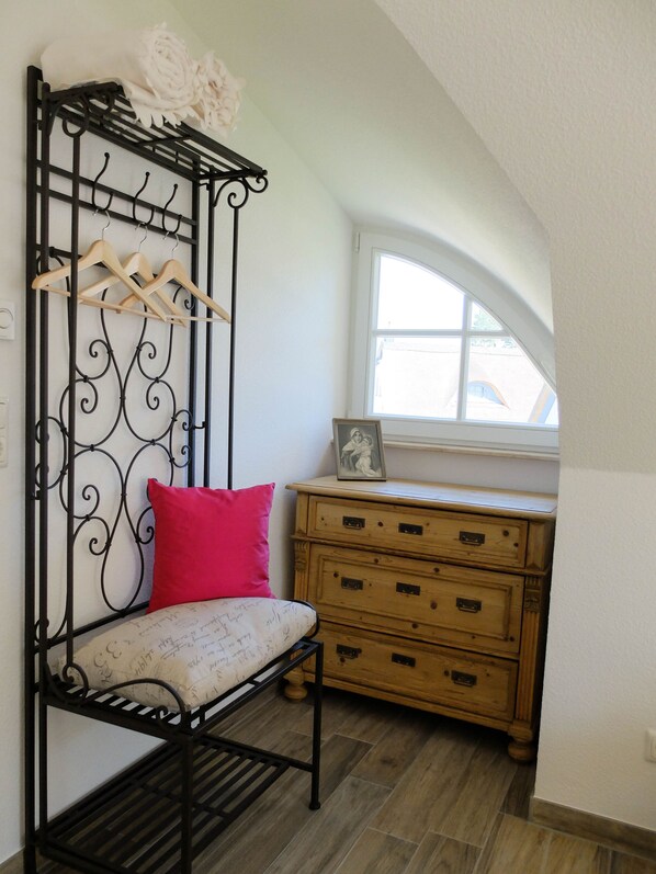 A room with a black metal bench with a cushion, a wooden dresser, and a window with a view.