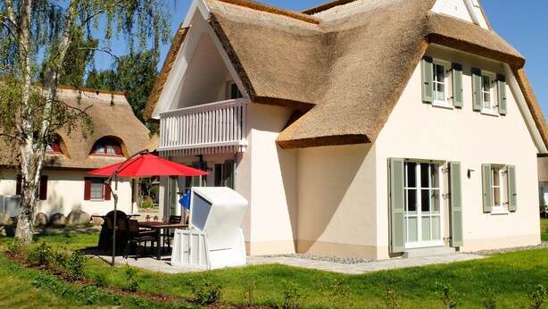 A house with a thatched roof, a balcony, and a red umbrella.