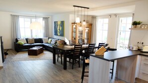 A modern living room with a sofa, dining table, and kitchen area.
