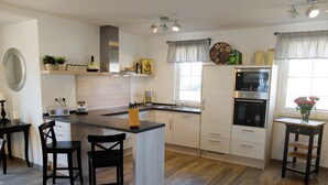 A modern kitchen with a central island, a microwave, and a stove. There are two black chairs and a small table with a vase of flowers.