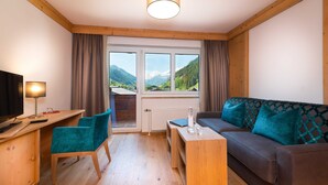 Ein Zimmer mit Holzboden, einer Couch, einem Schreibtisch, einem Sessel, einem Fernseher und einem Fenster mit Blick auf die Berge.