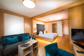 Ein modernes Hotelzimmer mit einer Couch, einem Bett, einem Fernseher und einer Holzbalkendecke.