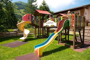 A playground with slides and climbing structures, surrounded by greenery and a building with a sign that reads 'Kinderland'. - Deluxe Stone Pine Room - Hotel Alpina **** (Rauris)