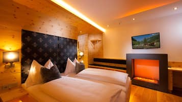 Habitación de hotel con techo de madera, chimenea, cama con ropa blanca y televisor montado en la pared.