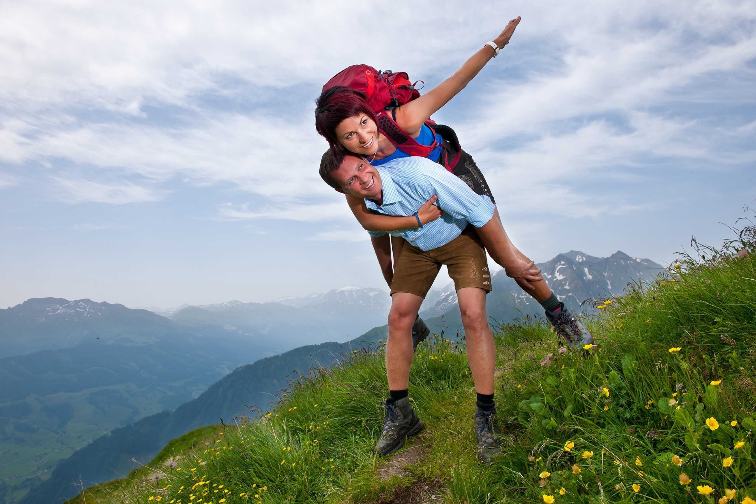 A couple on a mountain trail with a scenic view of mountains in the background.