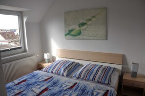 Un dormitorio con cama, mesita de noche, lámpara de noche, ventana y un cuadro colgado en la pared.