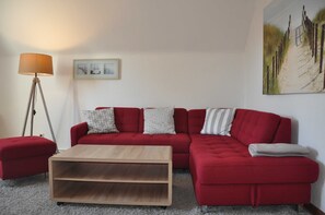 Un sofá rojo con almohadones estampados, una mesa de centro de madera, una lámpara de pie y un cuadro en la pared.