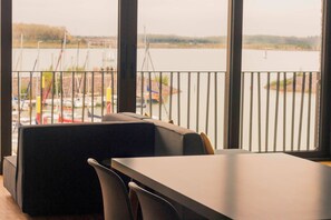A view from a room with a large window overlooking a marina with boats and a distant bridge. - The Generous (03) - Z1-THE HOUSE (Zwenkau)