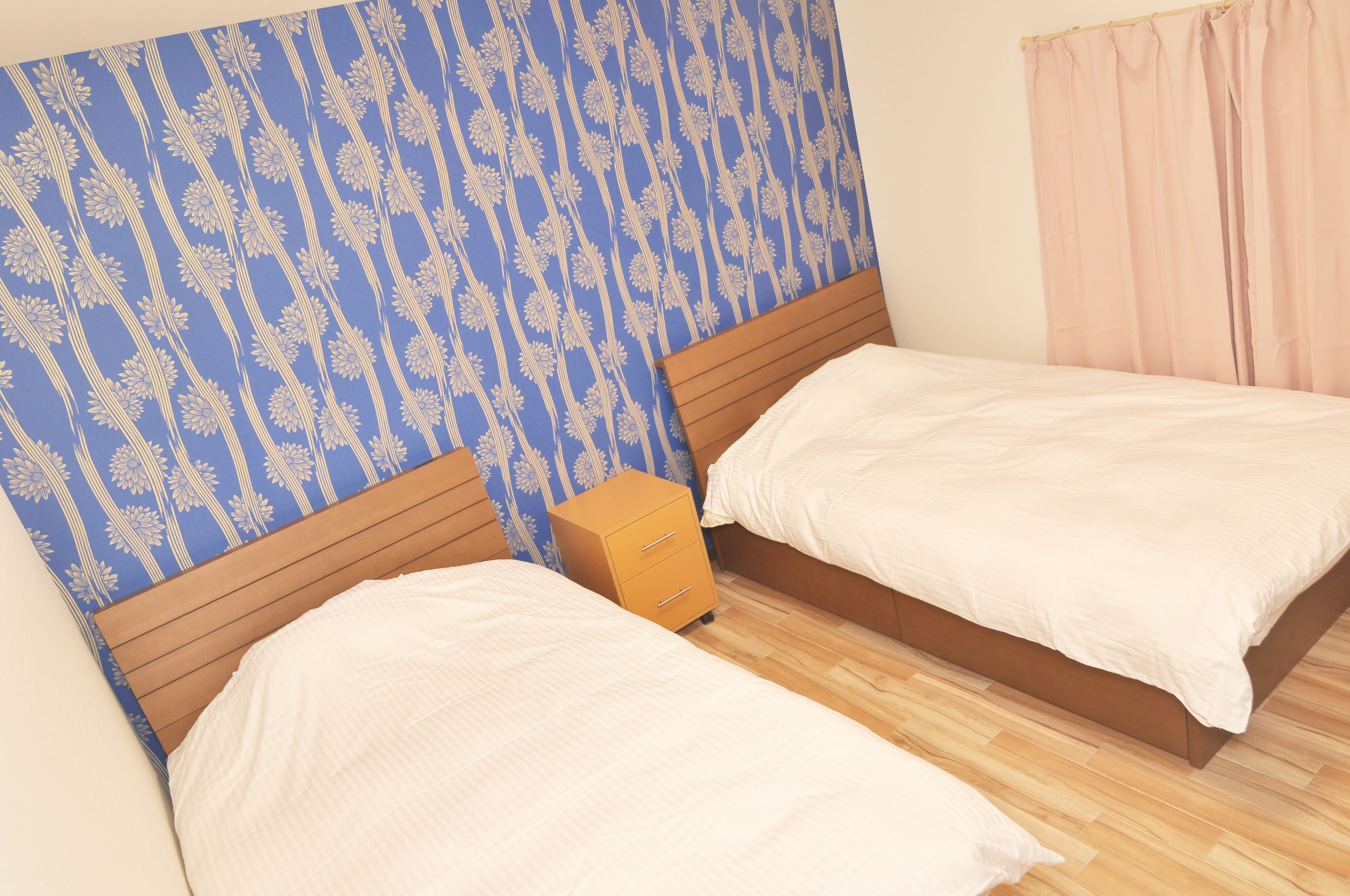 A bedroom with two beds, a wooden headboard, a nightstand, and a patterned wallpaper.