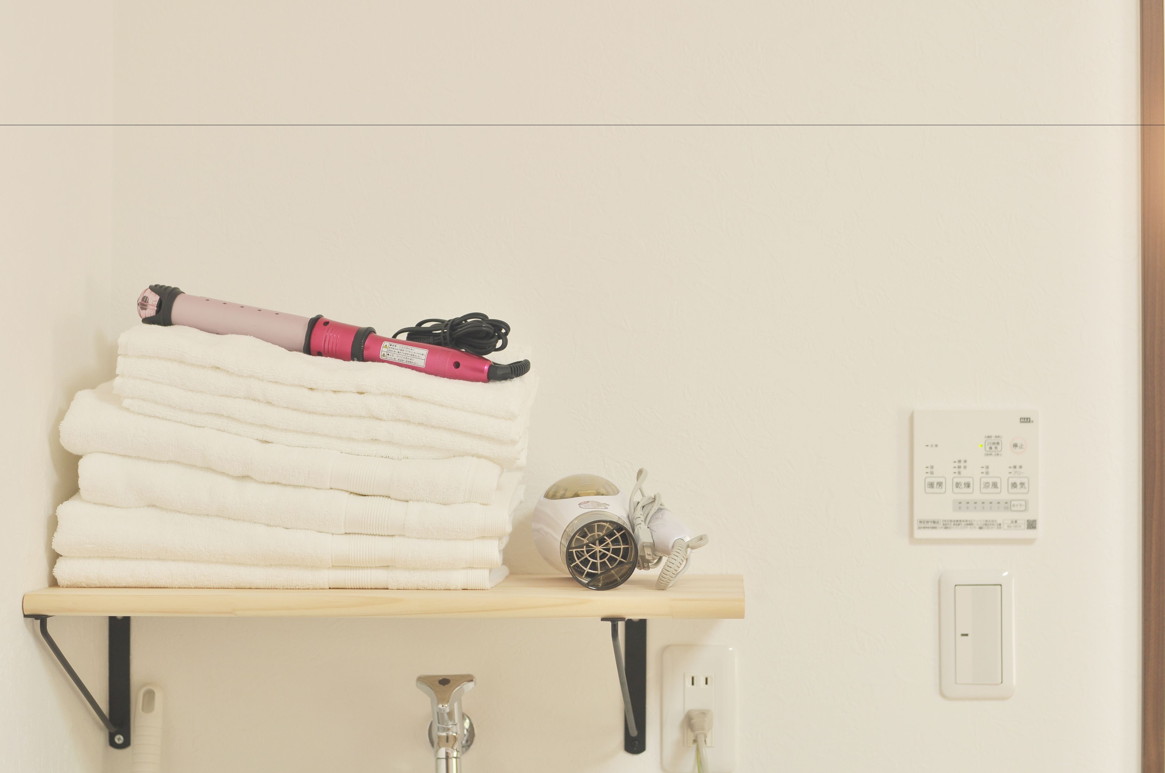 A bathroom with a towel rack holding folded towels, a hairdryer, and a pair of shoes.