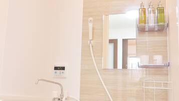 A modern bathroom with a bathtub, a handheld showerhead, a wall-mounted mirror, and a shelf with toiletries.