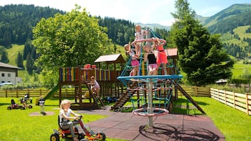 A playground with various play structures, including a climbing net, slides, and a wooden playhouse.