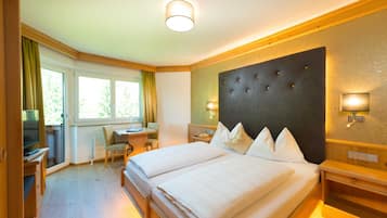 Una habitación de hotel con una cama grande, un escritorio, una silla, un televisor y un ventanal con cortinas.