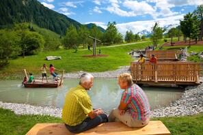 Een rivierlandschap met een houten brug, picknicktafels en een natuurlijke omgeving.