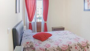 Ein Schlafzimmer mit Bett, Nachttisch, Fenster mit roten Vorhängen und einem Wandbild.