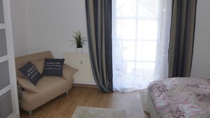 Een slaapkamer met een bed, een bank met kussens, een radiator en een raam met gordijnen.