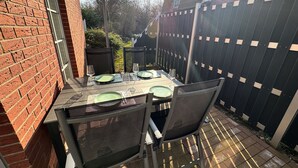 Een terras buiten met een tafel voor twee personen, stoelen en een bakstenen muur.