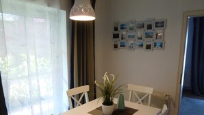 Een eetruimte met een witte tafel, vier stoelen, een hanglamp, een kamerplant en een muur met ingelijste foto's.