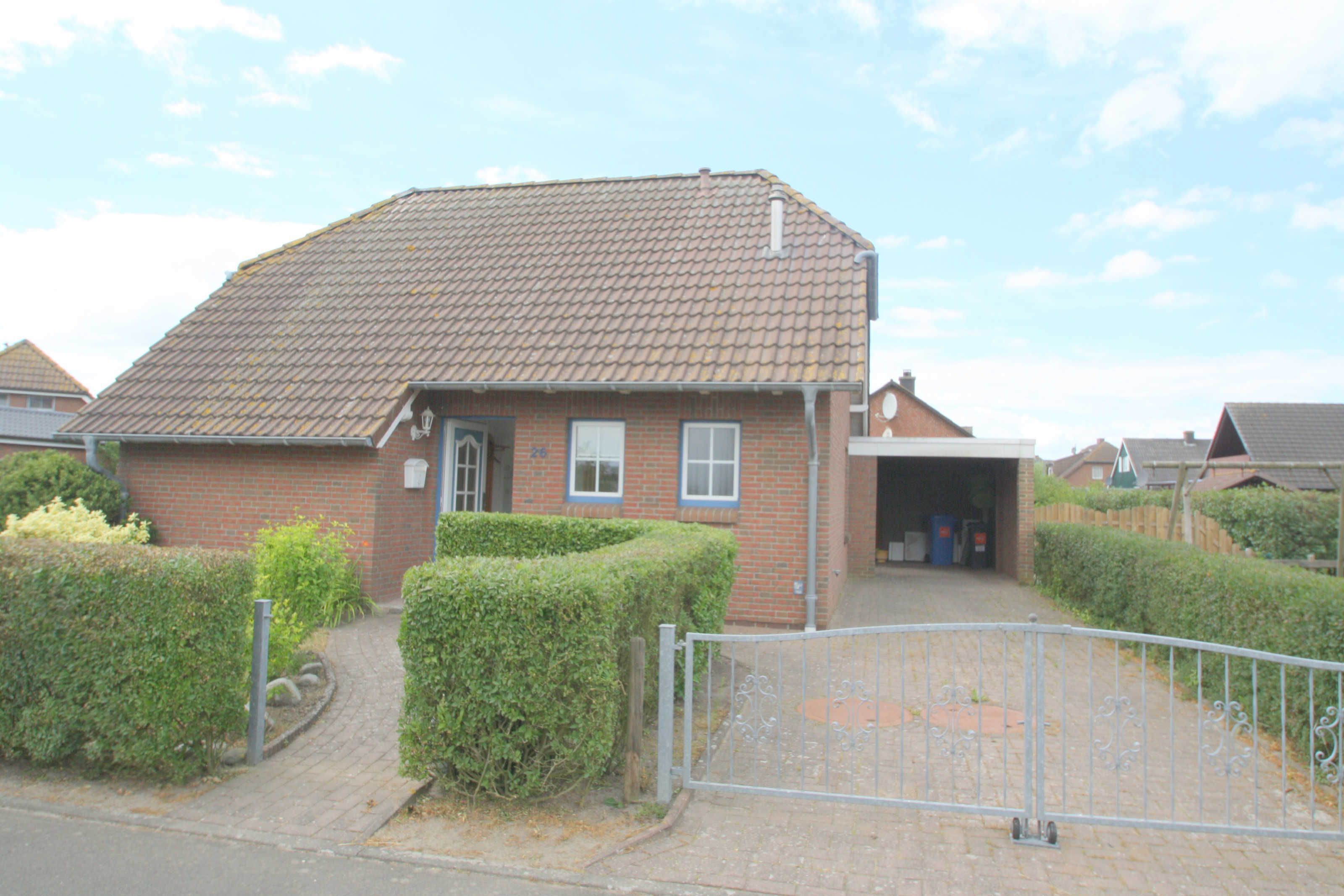 A brick house with a tiled roof, a gated driveway, and a small front yard with hedges.