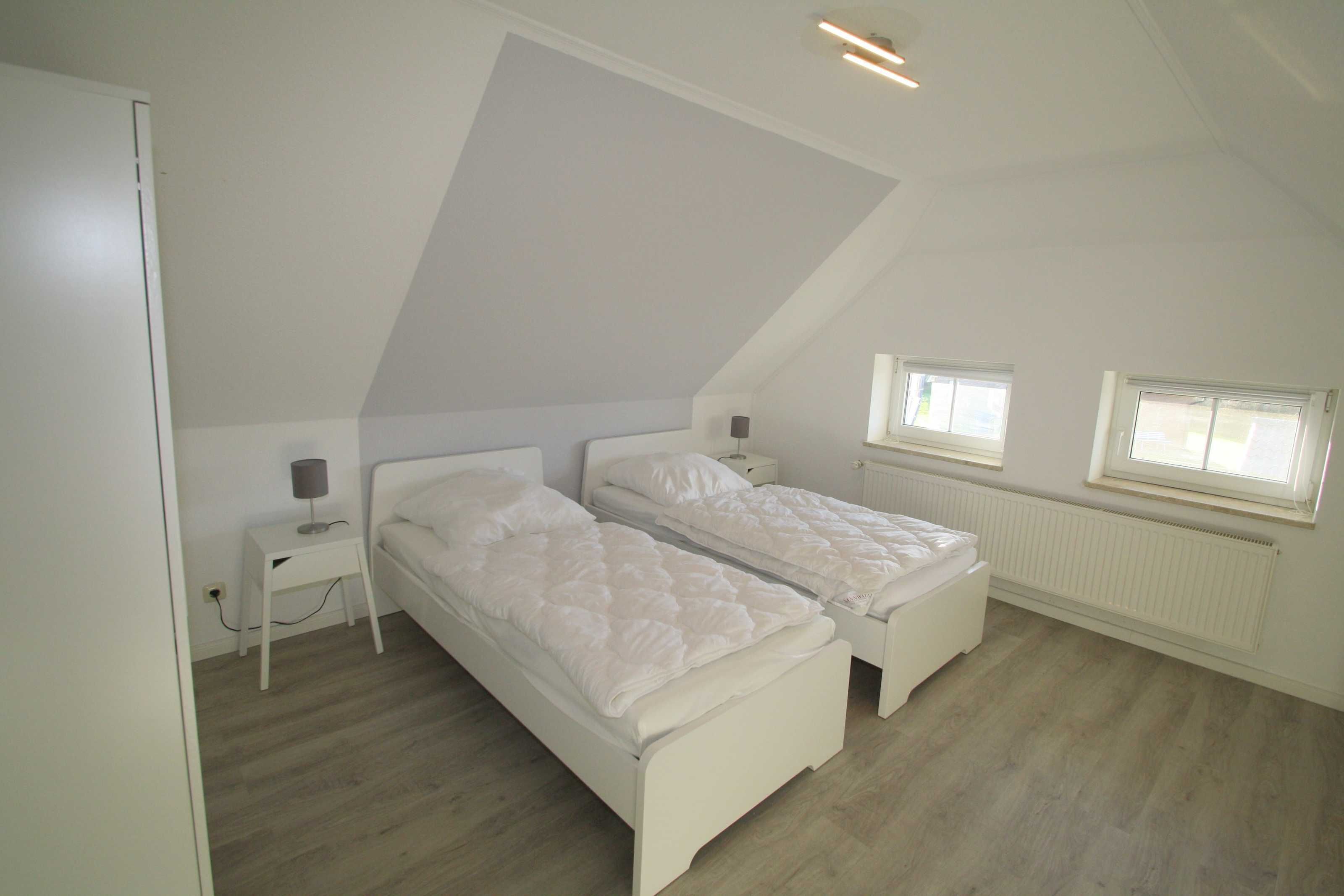 Un dormitorio con dos camas individuales, una mesita de noche pequeña con lámpara y un radiador.