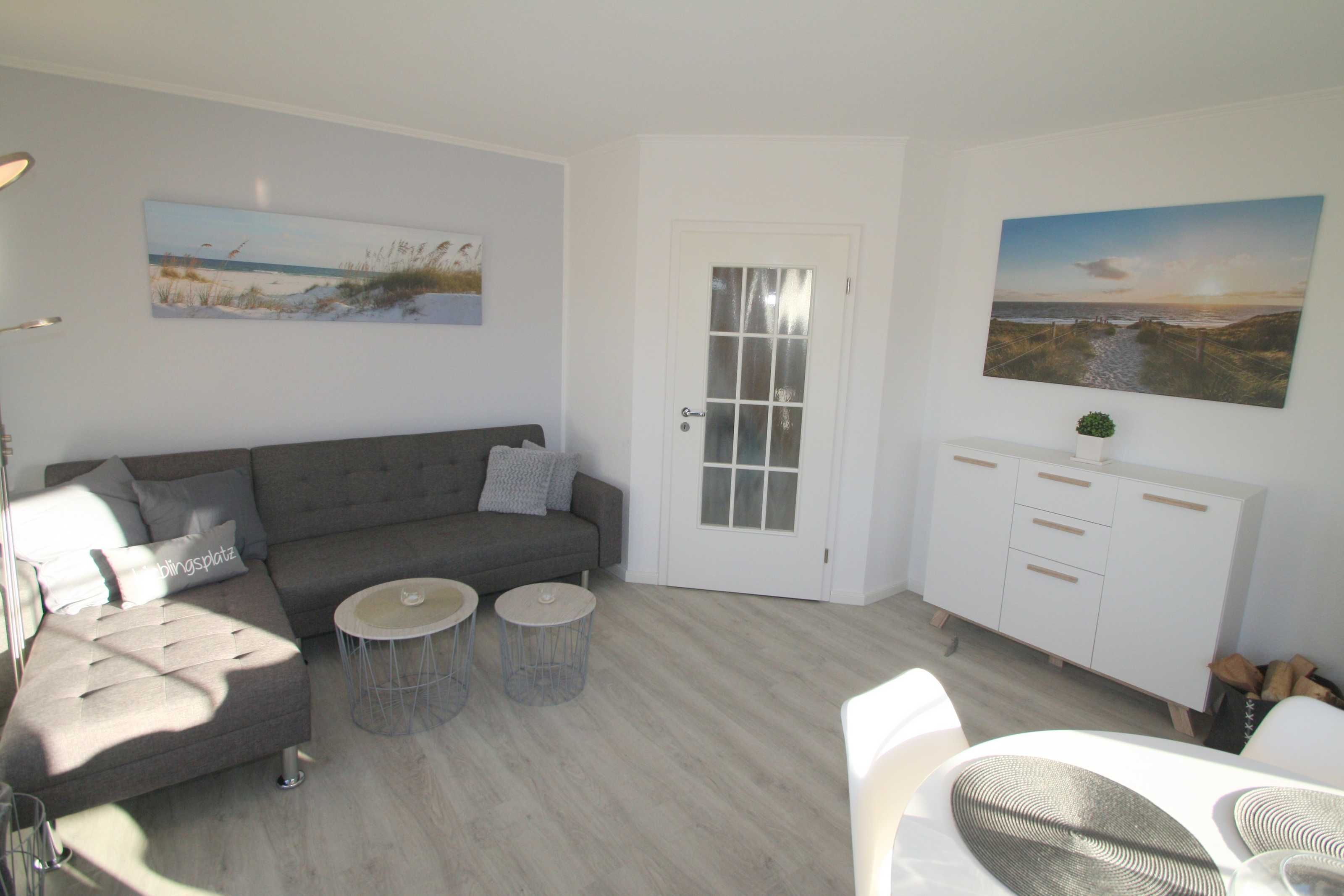 A modern living room with a grey sectional sofa, two round side tables, a white cabinet, and two wall-mounted paintings.