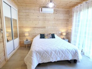 Un dormitorio con pared de paneles de madera, una cama con colcha blanca, dos lámparas de noche y un ventilador de techo.