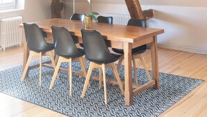 Un comedor con una mesa y sillas de madera, un tapete estampado y vigas de madera a la vista.