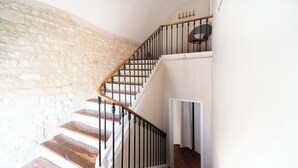Una escalera de madera con barandillas negras que conduce a un rellano con una silla y una puerta.