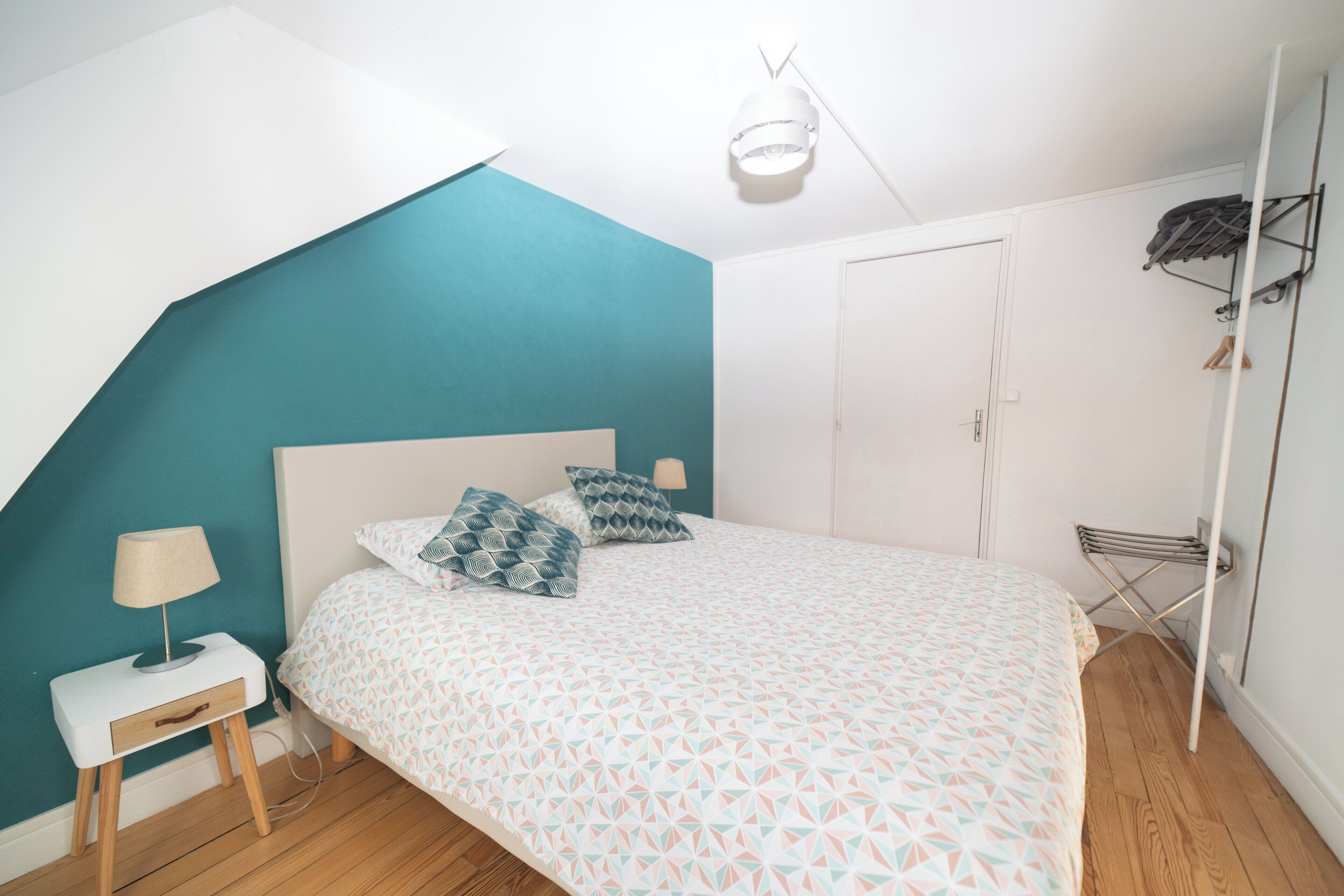 Une chambre à coucher comprenant un lit, une table de chevet, une lampe, une armoire et un porte-vêtements.