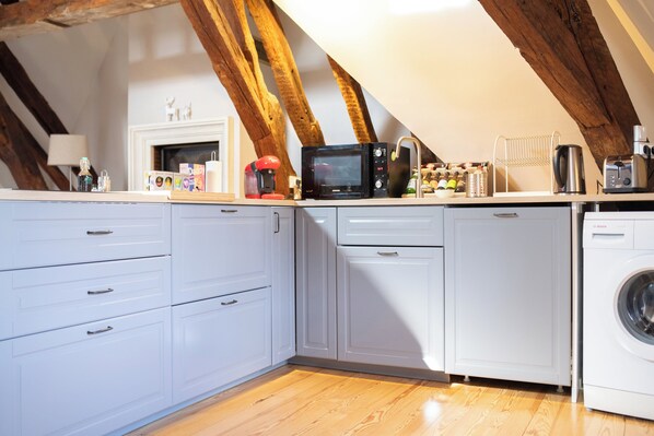 A kitchen with white cabinets, a microwave, a coffee maker, and a washing machine.