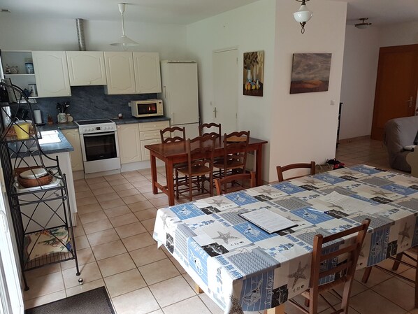 Cocina pequeña con armarios blancos, un microondas y una estufa. Hay una mesa de comedor con sillas y un mantel acolchado.