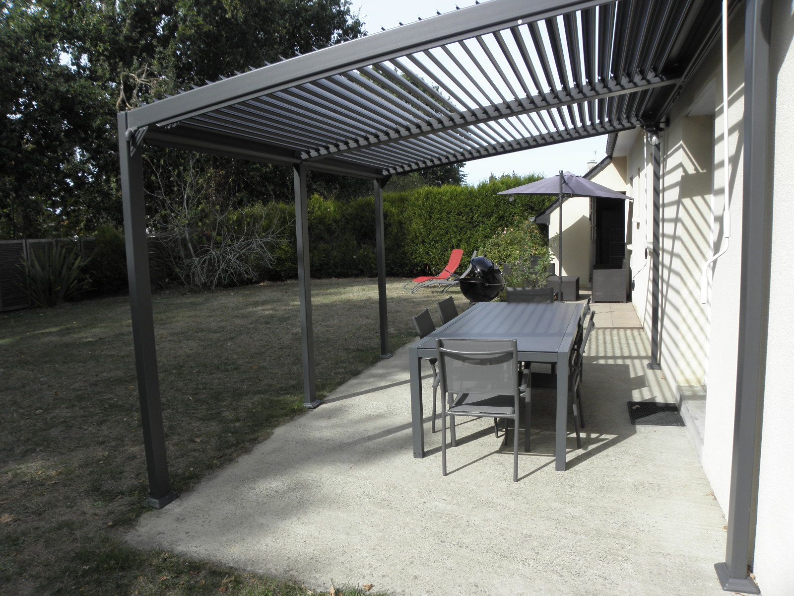 Un patio couvert avec une table et des chaises, un barbecue et une chaise rouge.