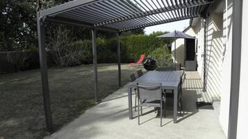Un patio couvert avec une table et des chaises, un barbecue et une chaise rouge.