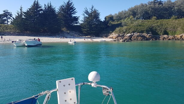 Un bateau sur un lac turquoise, avec une rive rocheuse et des arbres en arrière-plan.